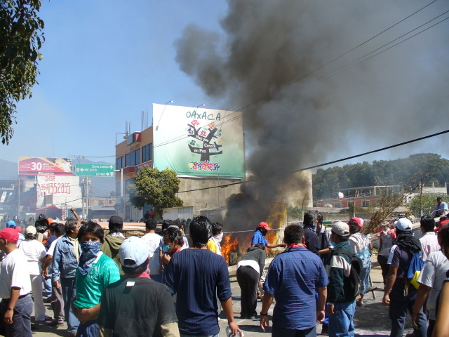 brandende autobanden met erachter het Oaxaca paz bord
